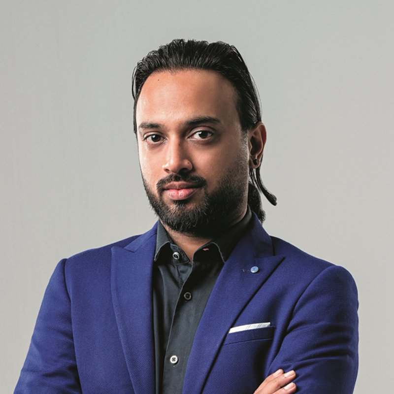 Headshot of a bearded man in a blue blazer with arms folded, grey backdrop