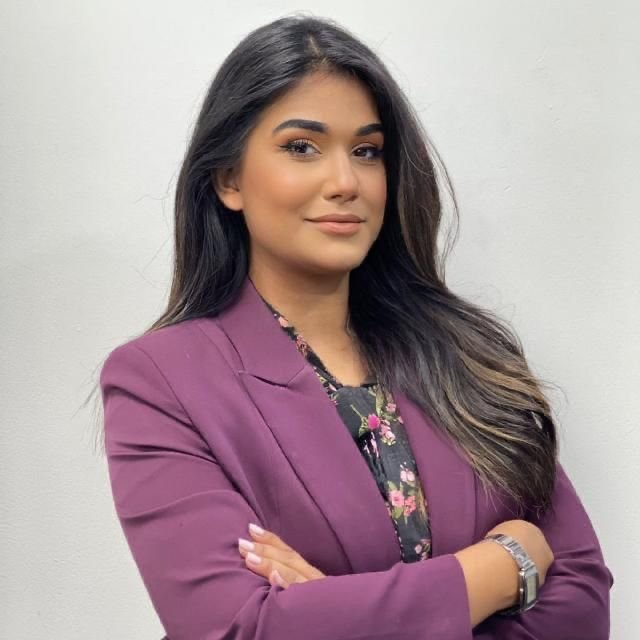 Team member in purple blazer with arms crossed on a light grey background
